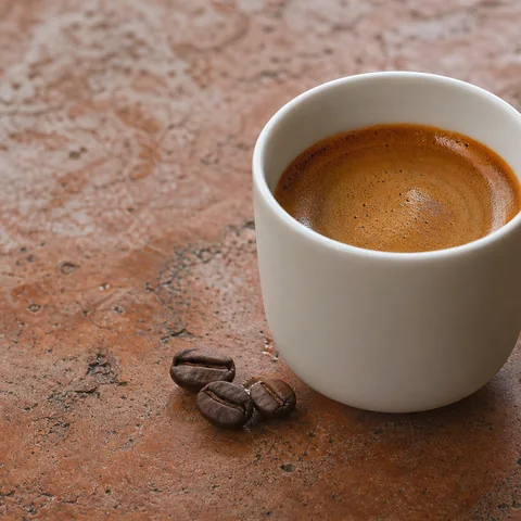 Fresh espresso surface, dark crema and roasted coffee grain in close detail.