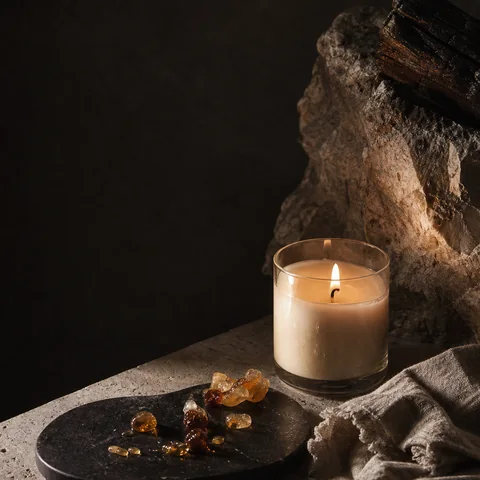 Muted amber candlelight reflected across resin, linen and dark stone.