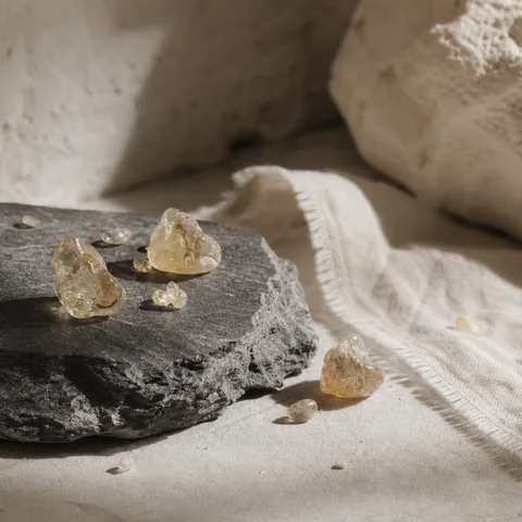 Raw frankincense resin tears on dark mineral stone with a fine trace of smoke.